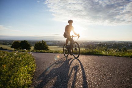 Ein Radfahrer fährt im Gegenlicht der Abendsonne mit seinem Gravelbike über einen asphaltierten Weg.