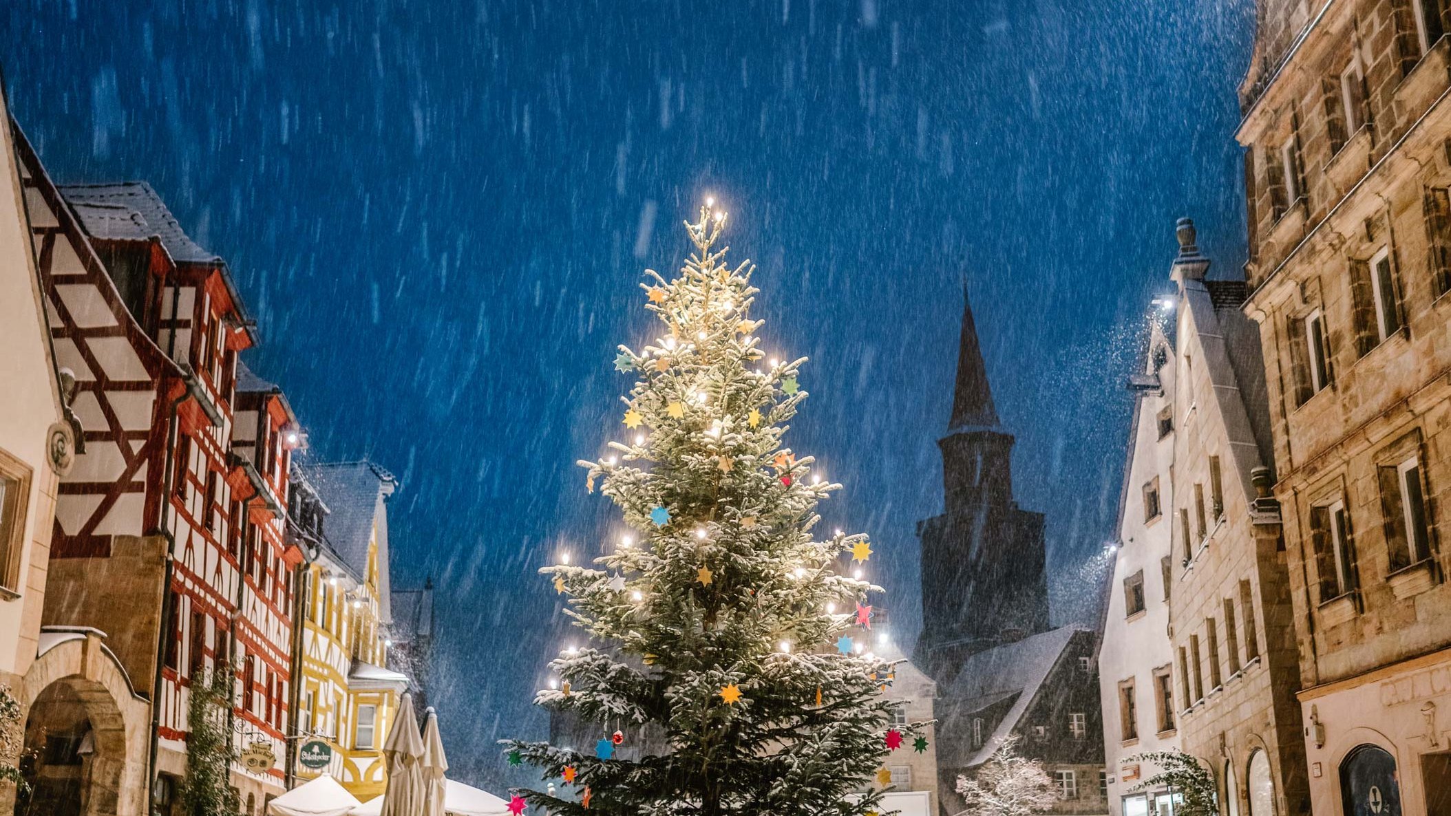 Geschmückter Weihnachtsbaum am Grünen Markt in Fürth, umgeben von Altstadthäusern im nächtlichen Schneefall.