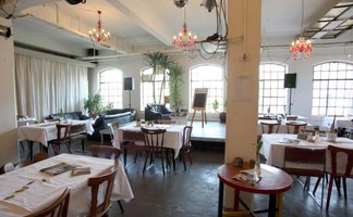 Gemütlicher Raum in der Kofferfabrik Fürth mit Holzstühlen, Bühne, Sofa und großen Industriefenstern