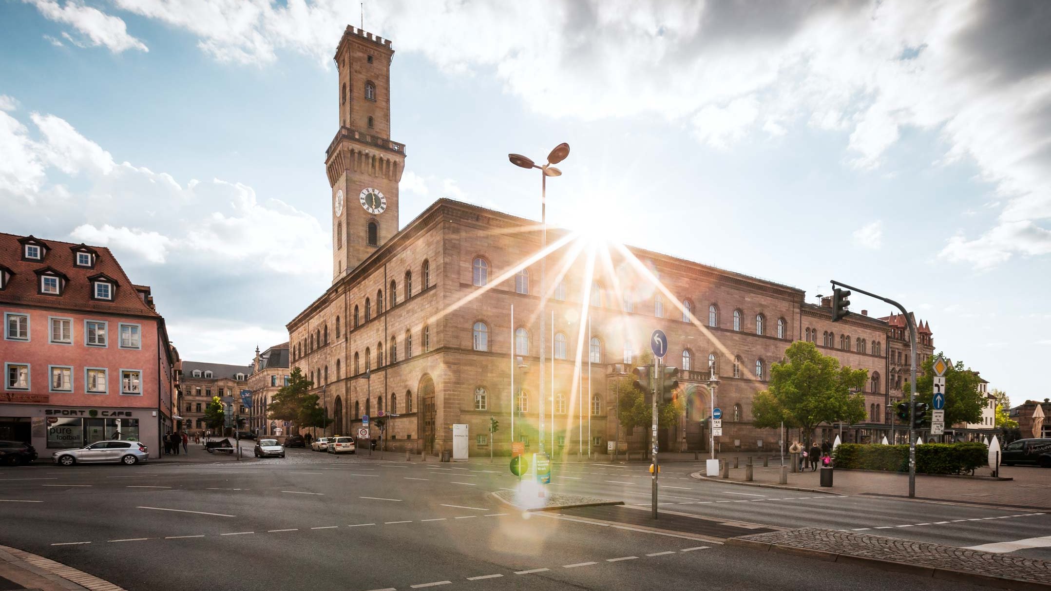 Das Fürther Rathaus mit majestätischem Turm, hinter dem die Sonne hell hervorscheint.