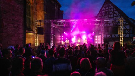 Band spielt auf dem Kirchenplatz, Publikum tanzt, hört Musik und feiert.