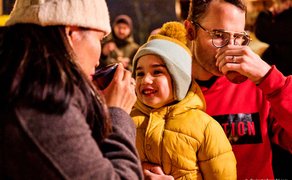 Eltern trinken Punsch mit ihrem kleinen Sohn auf dem Weihnachtsmarkt, gemütlicher Familienmoment.