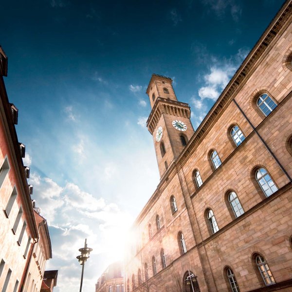 Von unten fotografierter Rathausturm mit Sonne dahinter, blauem Himmel und leichten Wolken.