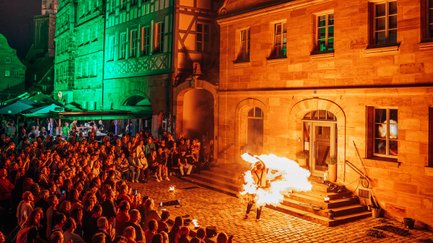 Menschen bestaunen eine Feuershow vor den grün beleuchteten historischen Häusern auf dem Grünen Markt.