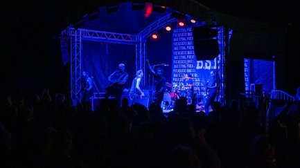 Blau beleuchtete Bühne am Lindenhain mit sechsköpfiger Band vor einem jubelnden Publikum