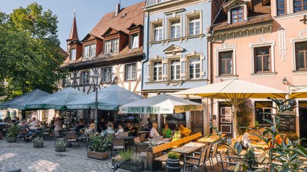 Fahrräder parken vor gemütlichen Restaurantterrassen und bunten Altbaufassaden im Sommer.