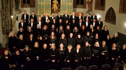 Großer Chor steht in Kirchenfront, einige mit Gesangsbüchern in der Hand.