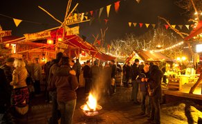 Besucher wärmen sich an einer Feuerschale auf dem Fürther Mittelaltermarkt und schlendern zwischen Ständen.