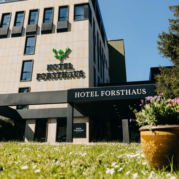 Ein markantes, mehrstöckiges Hotelgebäude mit heller Sandsteinfassade und grünem Forsthaus-Logo.