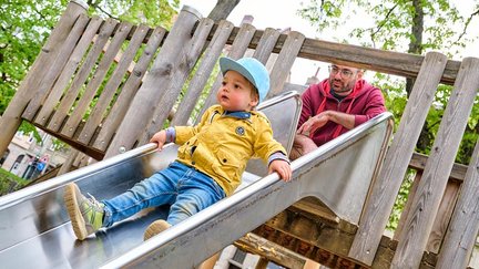 Ein Kind rutscht eine Rutsche hinunter, während der Vater von oben zusieht