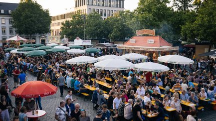 Festivalbesucher sitzen und stehen an Tischen und Ständen auf der Fürther Freiheit beim New Orleans Festival.