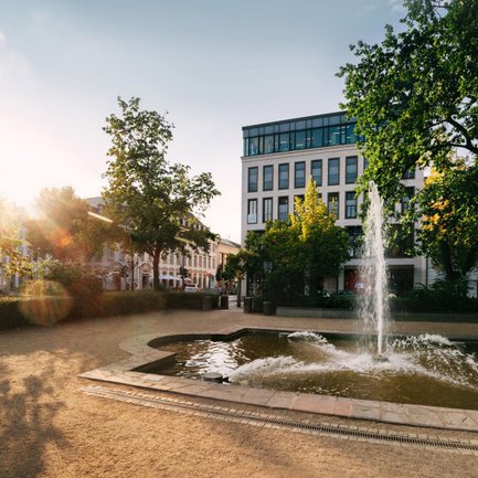 Blick auf den sprühenden Springbrunnen in der Dr.-Konrad-Adenauer-Anlage in Fürth mit der Neuen Mitte im Hintergrund