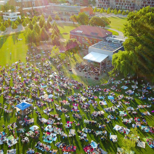 Viele Besucher sitzen auf Picknickdecken und blicken beim Südstadt Klassik Open Air auf die Bühne mit Orchester.