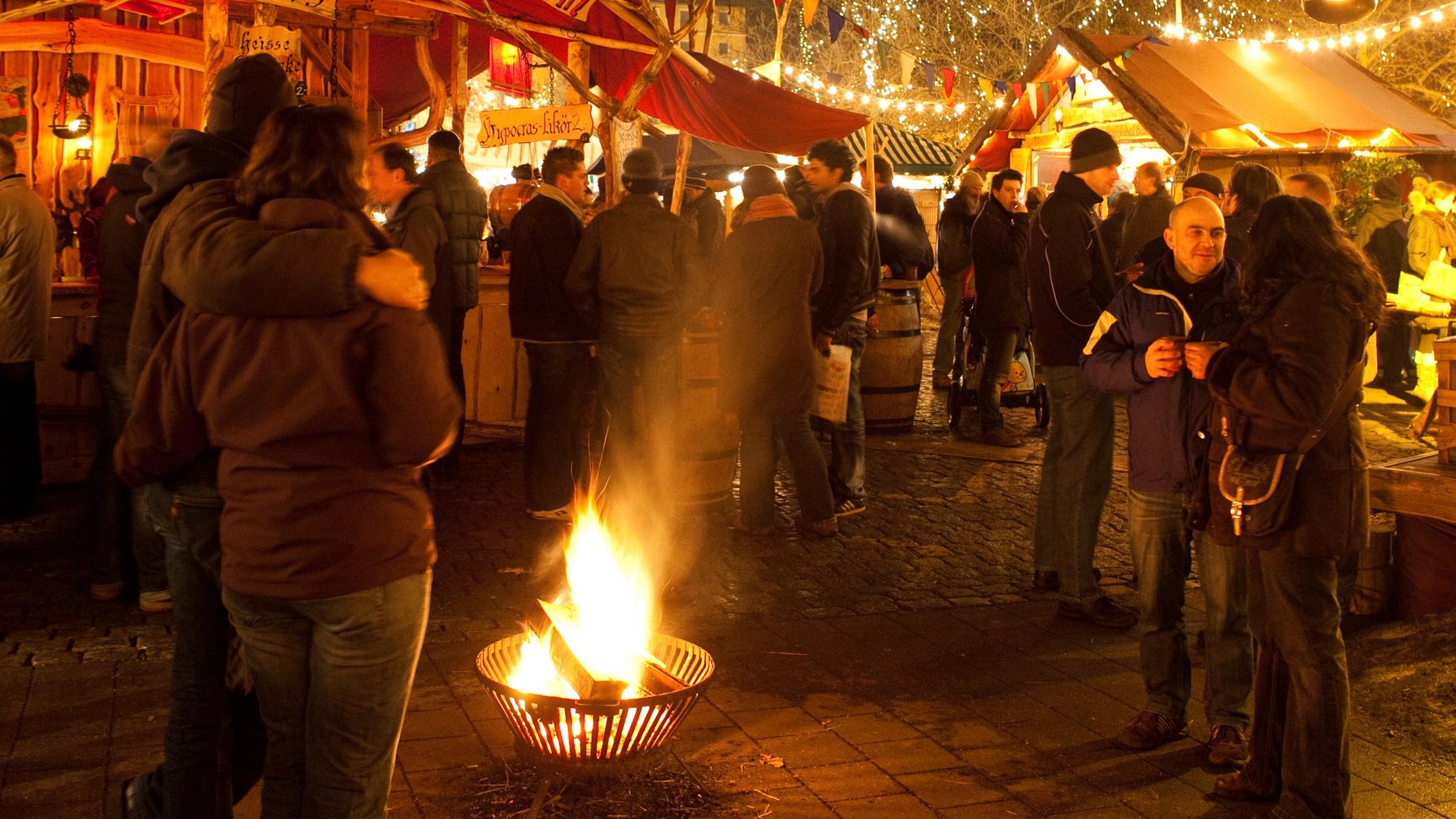 Abendliche Szene auf dem Mittelaltermarkt Fürth mit Lagerfeuer und festlich beleuchteten Hütten.