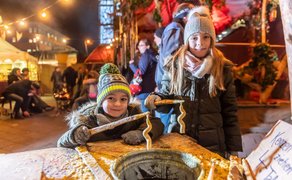 Zwei Kinder halten Kerzen über farbigem Wachs am Kerzenzieh-Stand des Mittelaltermarkts.