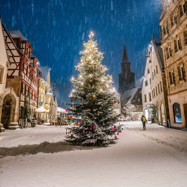 Geschmückter Weihnachtsbaum am Grünen Markt in Fürth, umgeben von Altstadthäusern im nächtlichen Schneefall.
