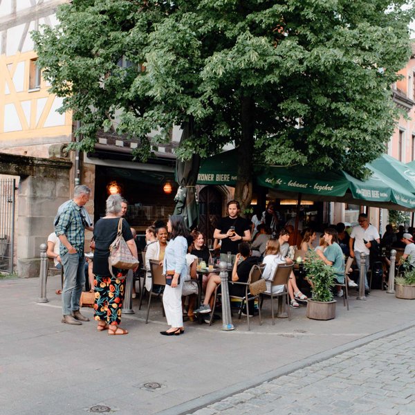 Menschen sitzen entspannt vor Cafés und Bars in der Gustavstraße und genießen das Stadtleben.