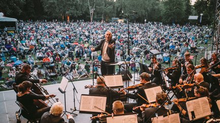 Dirigent leitet Orchester, Besucher auf Picknickdecken genießen die Classic Night unter freiem Himmel