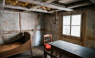 Historische Laubhütte in Fürth mit offenem Dach, Bett, Tisch, Stühlen und Deckenlampe.