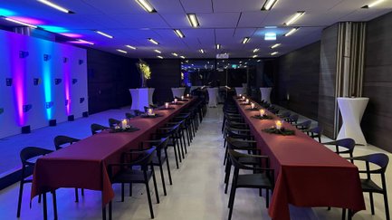 Großer Veranstaltungsraum im Ludwig Erhard Zentrum mit langgezogenen Tischreihen, roter Tischdecke, Kerzen und Bühne