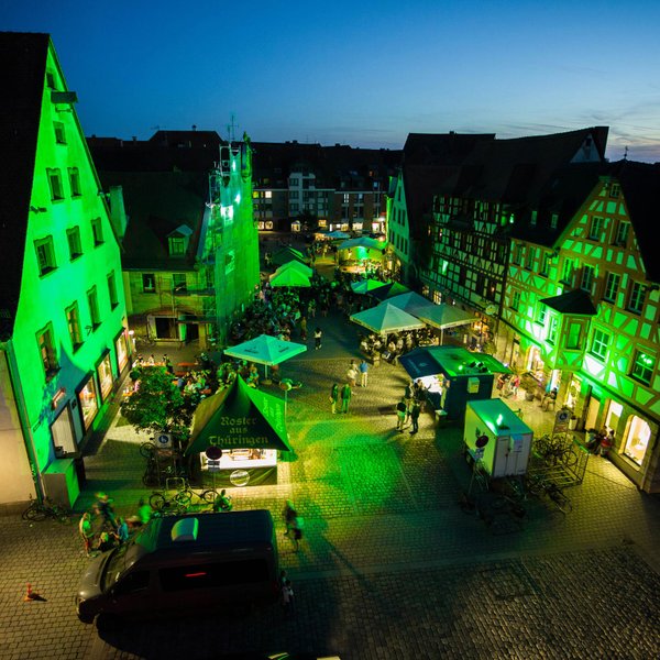 Historische Gebäude am Grünen Markt leuchten grün, Besucher sitzen an Bierbänken und Ständen.