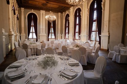 Saal im Logenhaus Fürth mit rund gedeckten weißen Tischen, Kerzen, Stuhlhussen, großen Fenstern und Kronleuchtern