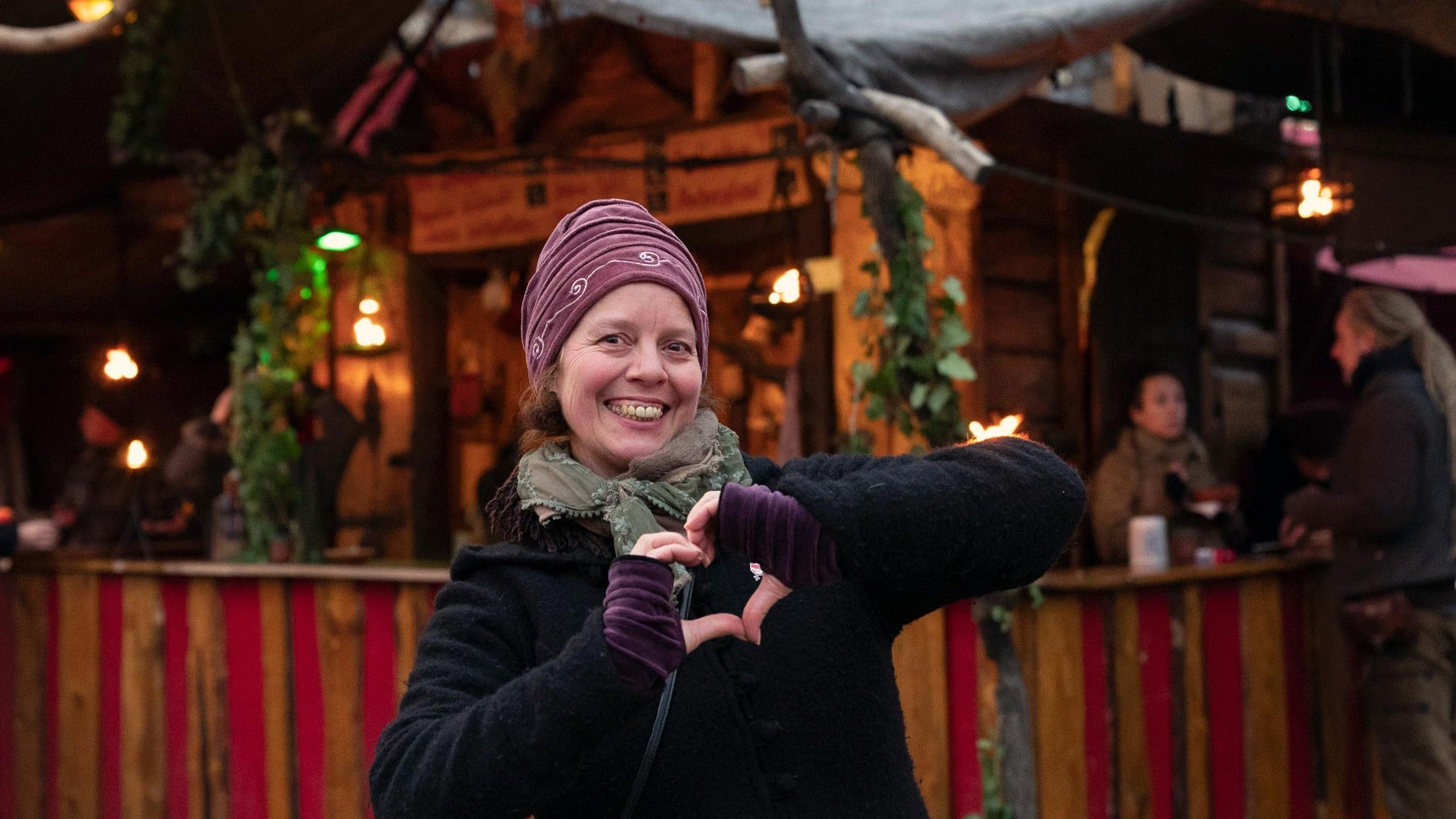 Edda steht vor einer der typischen Holzhütten auf dem Mittelaltermarkt in Fürth und lacht herzlich.