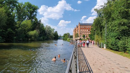 Badegäste schwimmen im Fluss Rednitz vor der Silhouette der historischen Kiß'kaltschen Häuser im Hintergrund