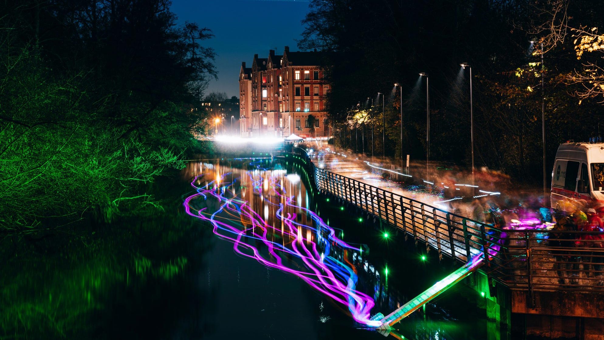 Uferpromenade in Fürth bei Nacht, farbig beleuchtet mit Reflexionen auf der Wasseroberfläche.