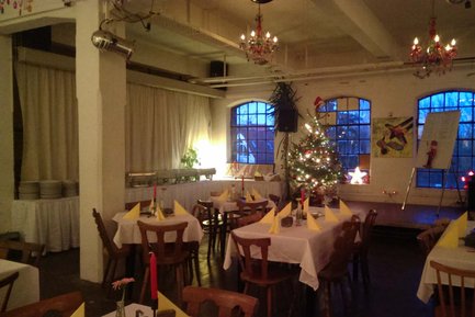 Abendliche Szene in der Kofferfabrik Fürth mit Weihnachtsbaum auf der Bühne und gedeckten Tischen