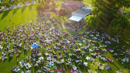 Viele Besucher sitzen auf Picknickdecken und blicken beim Südstadt Klassik Open Air auf die Bühne mit Orchester.