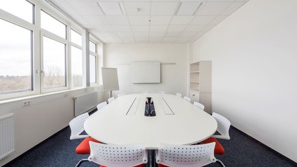 Heller Besprechungsraum mit rundem Tisch, 12 rot weißen Stühlen und Flipchart bei Neue Materialien