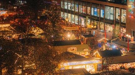 Blick von oben auf den Weihnachtsmarkt der Fürther Freiheit mit geschmückten Holzhütten und Mittelaltermarkt.