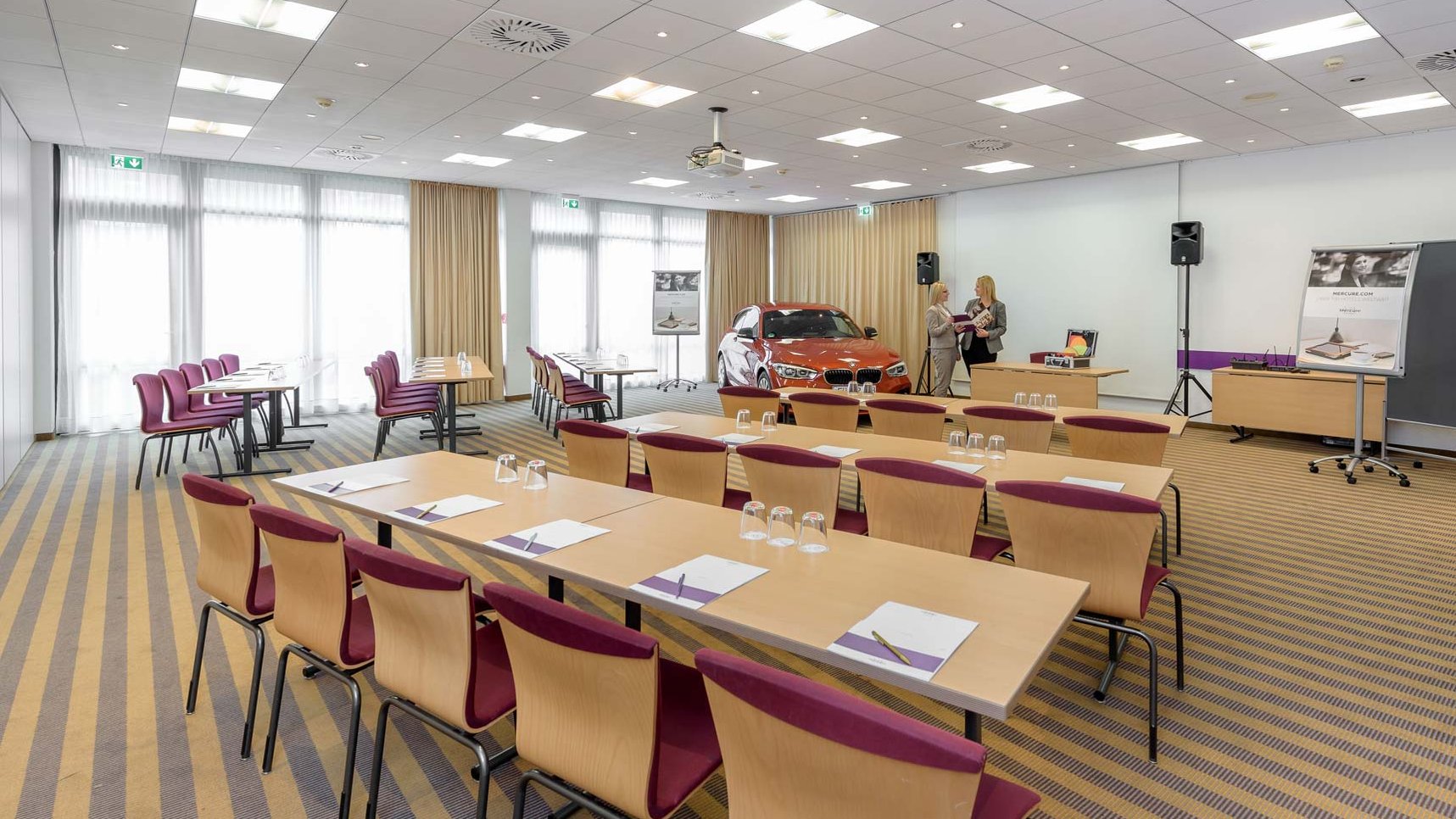 Tagungsraum im Mercure Fürth mit Reihen aus Tischen und Stühlen, Leinwand, Flipcharts und Zubehör