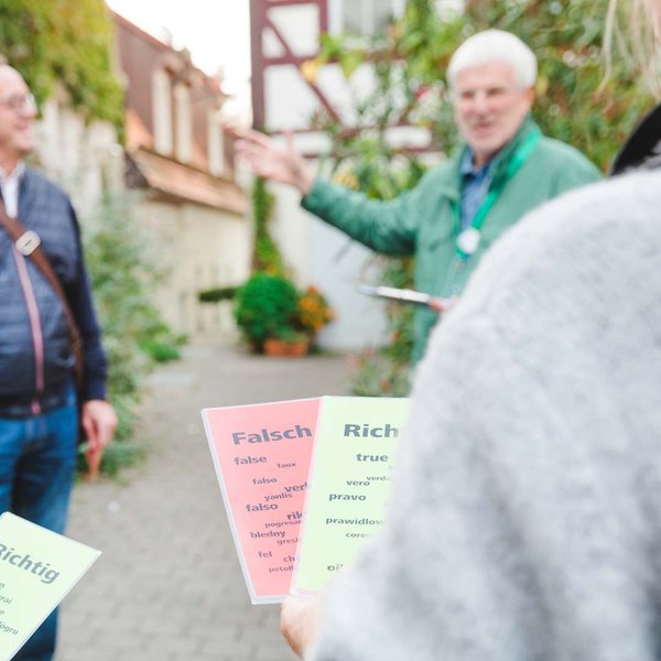 Teilnehmer einer Stadtführung halten rote und grüne Karten mit "Falsch" und "Richtig", während sie dem Stadtführer zuhören.