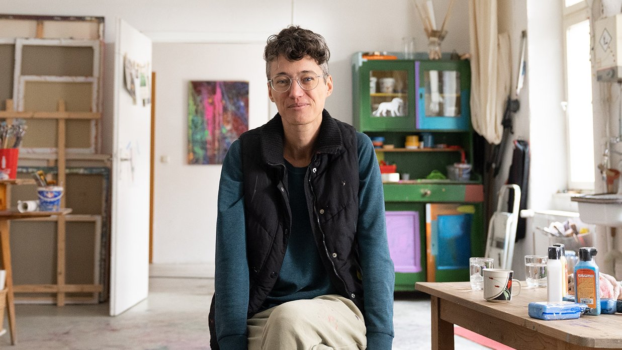 Sascha, Künstlerin aus Fürth, im Eingangsbereich ihrer Malwerkstatt, bereit für kreativen Austausch.