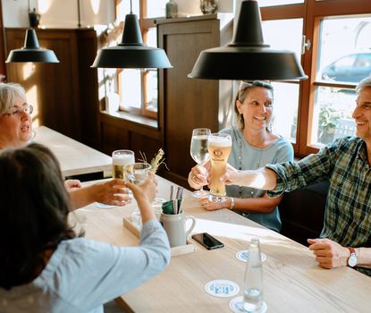 Gustavstraße Drei Frauen und ein Mann sitzen an einem Tisch und stoßen mit Ihren Gläsern an.