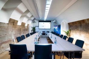 Seminar_5 Blick in den Seminarraum von Castros Bar in Fürth. In der Mitte steht ein großer, brauner Konferenztisch. Drum herum stehen Stühle. Hinten ist eine Leinwand auf die etwas projeziert wird.