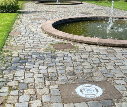 Selfie-Point im Rosengarten Auf dem Boden des Fürther Stadtparks, befindet sich eine weiße runde Markierung. Im Hintergrund sind Springbrunnen und die Auferstehungskirche zu sehen.