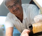 Käse Langer Ein Mann mit einem weißen Oberteil, hält ein Stück Käse in das Bild.