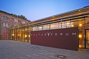 Vom Schlachthof zum Kulturtempel Blick auf den Eingangsbereich, des im dunkeln beleuchteten Kulturforums. Das große, rote Schild mit der mit der Aufschrift steht dabei im Vordergrund.