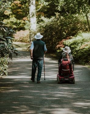 annie-spratt_unsplash Mann mit einem Gehstock und Frau im Rollstuhl spazieren durch den Park.