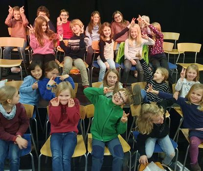 Kinder- und Jugendkantorei Viele Kinder sitzen auf Stühlen und schneiden für das Foto Grimassen.