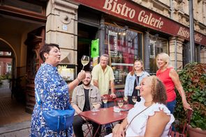 Dämmerschoppen Die Stadtführerin spricht zu den Teilnehmern der Dämmerschoppen-Führung. Dabei hält sie ein Weinglas in der Hand. Im Hintergrund ist die Bistro Galerie Fürth zu sehen.
