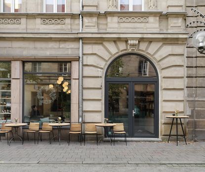 Kaffeesurium außen Blick auf den Eingang und den Außenbereich des Kaffeesurium. Es sind Stühle und Tische zu sehen.